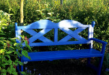 Niebieska ławka na końcu ogrodu. Siedząc na niej można oglądać całą rabatę bylinową wokół zelonej polany i zachód słońca.