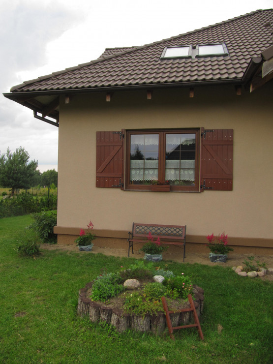 Przed kuchennym oknem iście wiejskie klimaty: samodzielnie wykonane okiennice, ławka oraz ozdobny klomb z drabinką