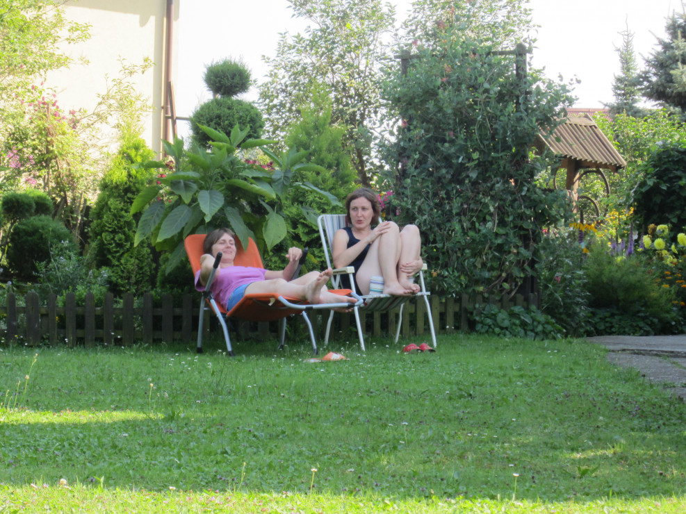 Siostra Ania z Bratową Agnieszka odpoczywają  w ogrodzie gdzie widać ciekawie przycięte krzewy.